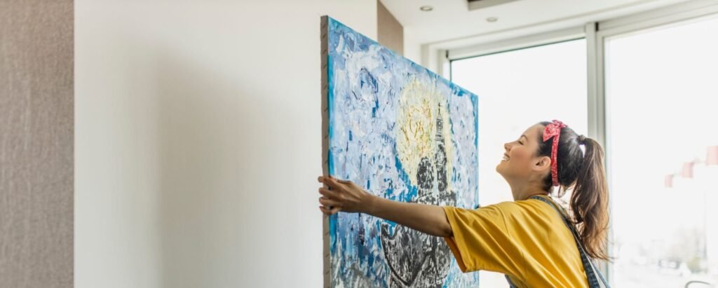 young woman hanging art picture on wall and decorating living room